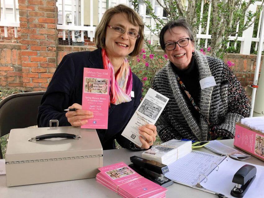 Two women smiling sitting at table holding pink tickets and tour guide