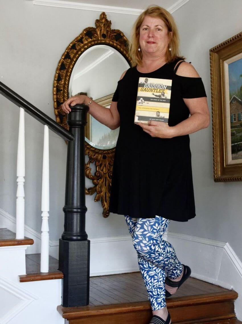 Christie Frazier standing on stairs holding Gridiron Gauntlet book